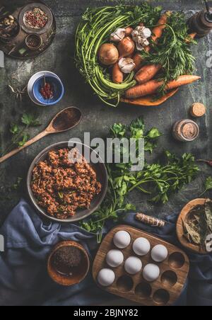 Tasty cooking. Flavored minced meat in wooden bowl with vegetables , herbs and spices ingredients, cooking spoon on dark rustic background. Top view.