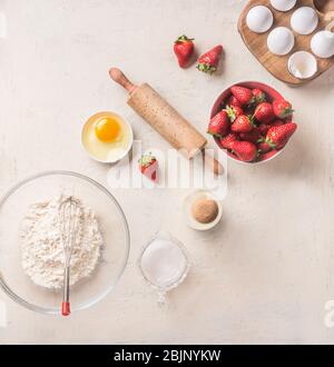 Baking background with flour, eggs,rolling pin and  strawberries on white kitchen desk background, top view. Flat lay. Sweet food. Bake ingredients an Stock Photo