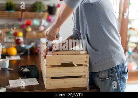 Man drilling wooden crate with power tool at home Stock Photo