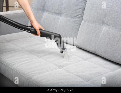 Woman cleaning couch with vacuum cleaner at home Stock Photo