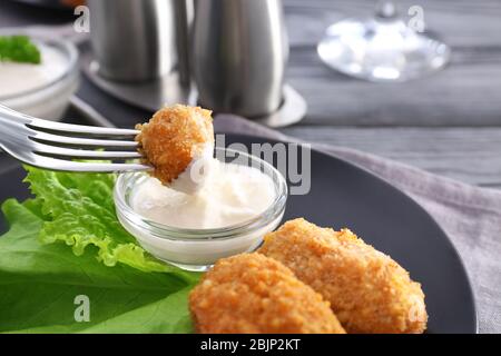 Dipping piece of salmon croquette into gravy boat with sauce on plate Stock Photo