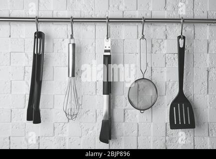 Kitchen utensils hanging on rack against white wall Stock Photo