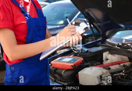 Young female mechanic with clipboard near car in body shop Stock Photo