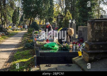 Ladies make graves neatly at Rakowicki cemetery in Krakow, Poland 2019. Stock Photo