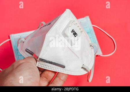 Wuhan, China - April 21 2020: White mask 3m with a valve on a homogeneous pink background during the coronavirus pandemic. Man hand holding mask 2021. Stock Photo