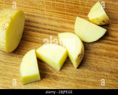 A half white potato and five potato pieces with skin on on a wooden chopping board Stock Photo