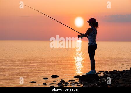 Woman fishing on Fishing rod spinning at sunset background Stock