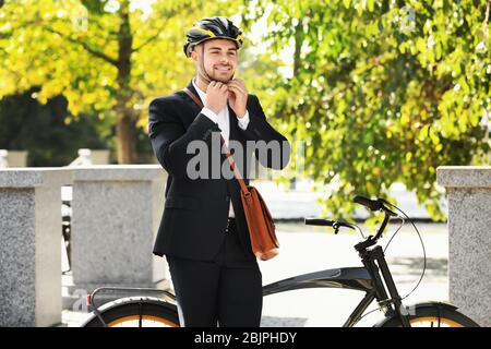 Young handsome businessman putting on bicycle helmet outdoors Stock Photo
