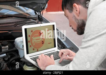 Young male mechanic using computer diagnostic while repairing car Stock Photo