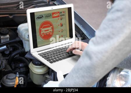 Young male mechanic using computer diagnostic while repairing car Stock Photo