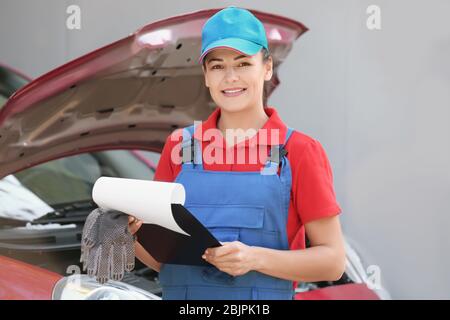Young female mechanic with clipboard near car outdoors Stock Photo