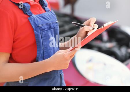 Young female mechanic with clipboard near car outdoors Stock Photo