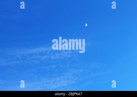 A half moon in a clear blue sky in Manchester, England Stock Photo