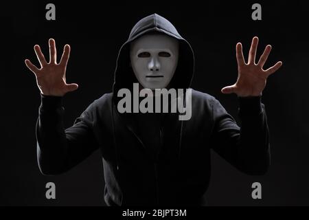 Hacker in mask working with virtual screen on dark background Stock Photo