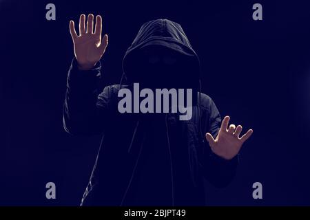 Hacker in hood working with virtual screen on dark background Stock Photo