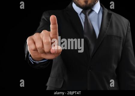 Businessman pushing button on virtual screen against dark background Stock Photo