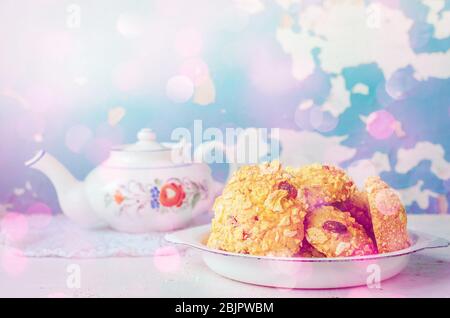 Homemade cornflakes and raisins cookies with tea pot on old wall background. Freshly baked corn flake cereal cookies in rustic style. Selective Focus. Stock Photo