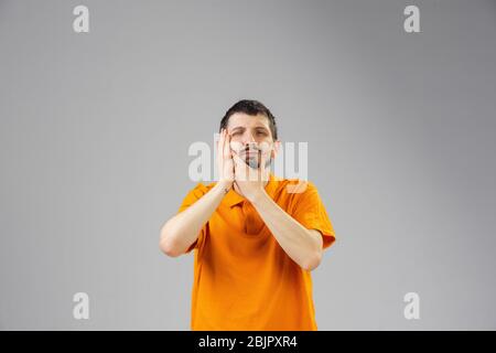 Young caucasian man suffers from teethache, feels sick, ill and weakness isolted on gray studio background. Symptoms of desease or unhealthy lifestyle. Sickness, ilness, sad and upset. Copyspace. Stock Photo