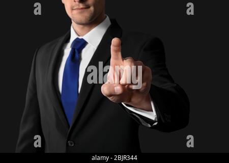 Businessman pushing button on virtual screen against dark background Stock Photo