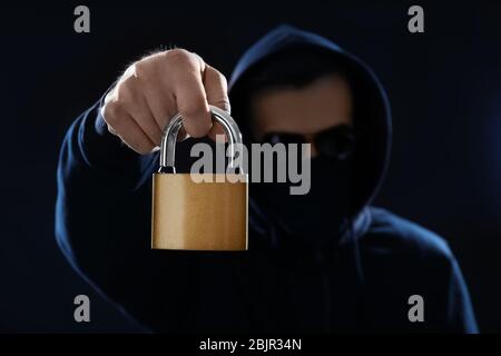 Hacker in mask holding lock on dark background Stock Photo