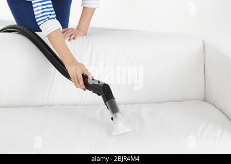 Woman removing dirt from sofa by using vacuum cleaner Stock Photo