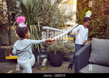 Afro-American boy and girl playing in the backyard with plastic swords, active Stock Photo