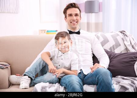 Father and son in shirts with bowties sitting on sofa at home Stock Photo