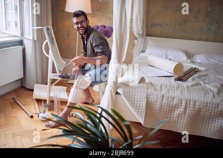 Young smiling man artist painting with oil on canvas picture. Stock Photo