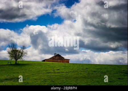 Red Barn sits on a green hillside under cloudy skies in rural Tennessee. Stock Photo