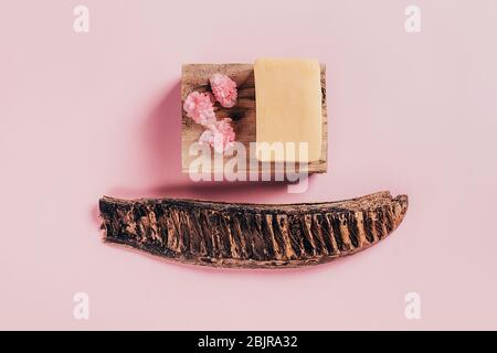 Piece of soap on wooden bar with begonia flowers on pink paper background. Health and beauty concept. Stock Photo