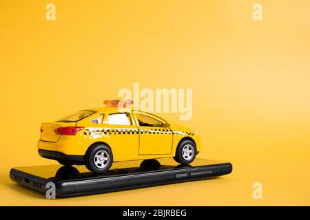 Urban taxi mobile online application concept. Toy yellow taxi car model. Hand holding smart phone with taxi service app on display. Mock up with copy