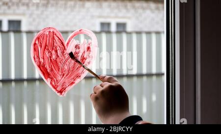 hands of a girl with a paintbrush painting red heart on a window, copy space for text, stay home Stock Photo