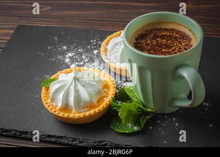 Lemon tart with mint leaves and a cup of cappuccino with chocolate topping. Stock Photo
