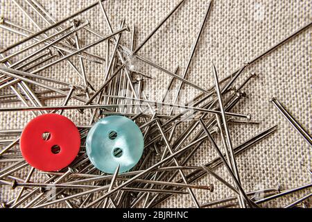 Red and blue button with seamstress pins on sack clothes. Close up. Stock Photo