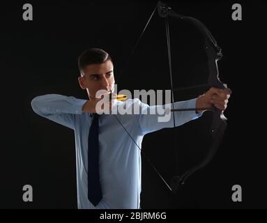 Young businessman practicing archery on dark background Stock Photo