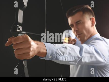 Young businessman practicing archery on dark background Stock Photo