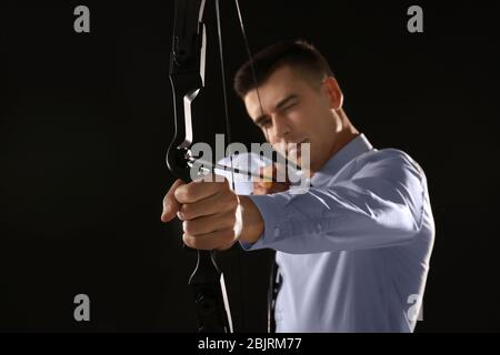 Young businessman practicing archery on dark background Stock Photo