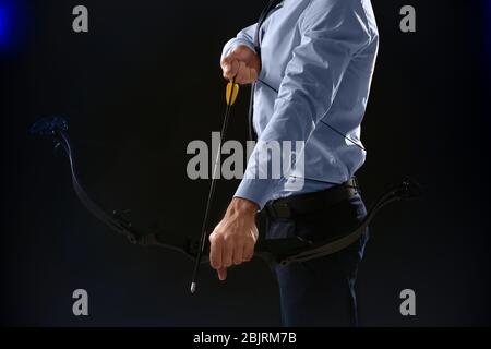 Young businessman practicing archery on dark background Stock Photo