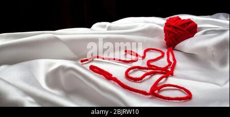 white silk fabric with bends and a red knitted heart with nicknames for Valentine's Day, copy space Stock Photo