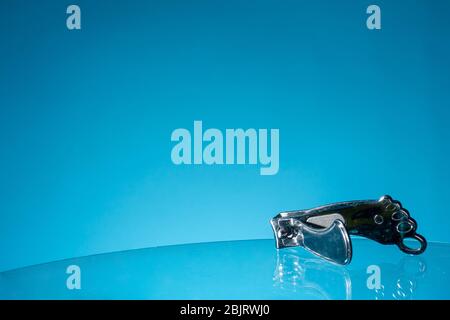 Metal nail clippers in the form of foot feet on glass blue background, close up, copy space Stock Photo