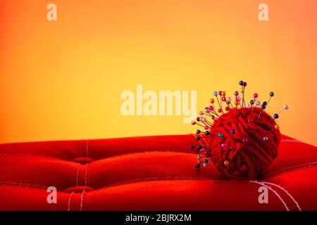 a red skein of thread stuck a lot of needles on red leather on an orange background. close up copy space Stock Photo