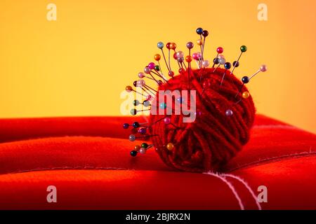 a red skein of thread stuck a lot of needles on red leather on an orange background. close up copy space Stock Photo
