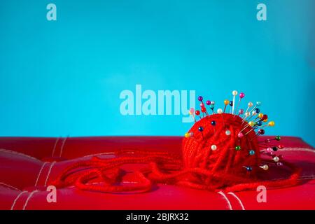 a red skein of thread stuck a lot of needles on red leather on a blue background. close up copy space Stock Photo