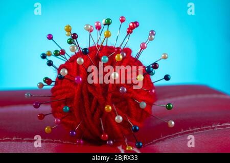 a red skein of thread stuck a lot of needles on red leather on a blue background. close up copy space Stock Photo