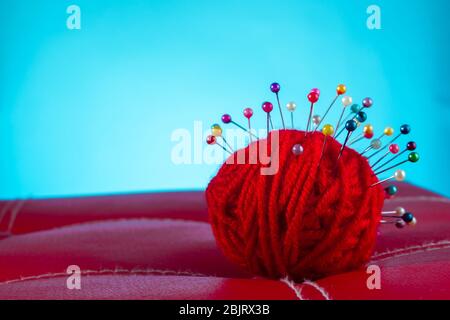 a red skein of thread stuck a lot of needles on red leather on a blue background. close up copy space Stock Photo