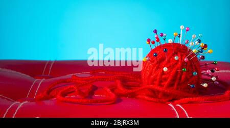 a red skein of thread stuck a lot of needles on red leather on a blue background. close up copy space Stock Photo