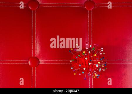 a red skein of thread stuck a lot of needles on red leather. close up copy space Stock Photo