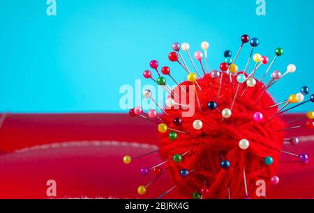a red skein of thread stuck a lot of needles on red leather on a blue background. close up copy space Stock Photo