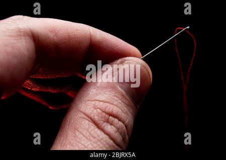 needle in hand with red thread on a black background Lush Lava backlight. close up copy space Stock Photo