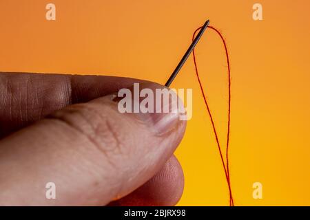 needle in hand with a red thread on a Lush Lava background. close up copy space Stock Photo